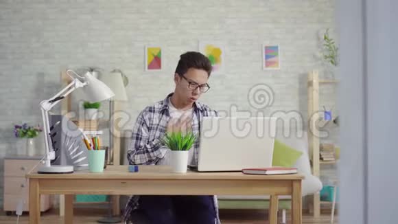 一个穿着哮喘衬衫的亚洲年轻人喜欢坐在笔记本电脑前咳嗽的喷雾视频的预览图