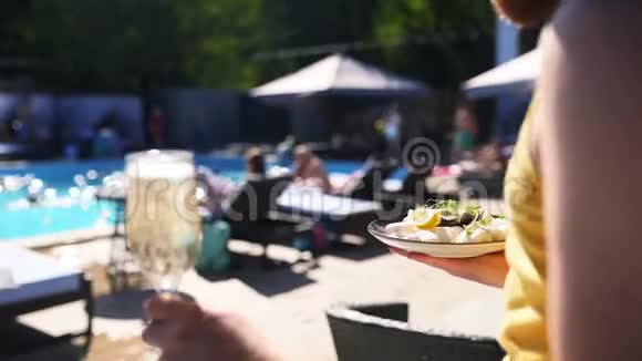 服务员在豪华游泳池附近的托盘上端着牡蛎和扇贝香槟或汽酒视频的预览图