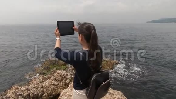 一位背着背包的游客在他的平板电脑上拍摄了一段海浪的视频视频的预览图