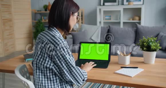 微笑的女孩用带绿色屏幕的笔记本电脑在家里工作视频的预览图