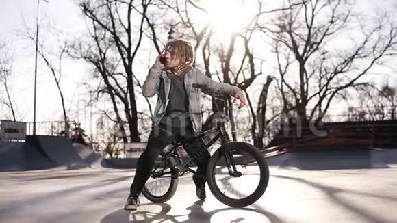快乐英俊的带着可怕的屁股的十几岁男孩的肖像骑着BMX自行车时使用手机微笑着发信息视频的预览图