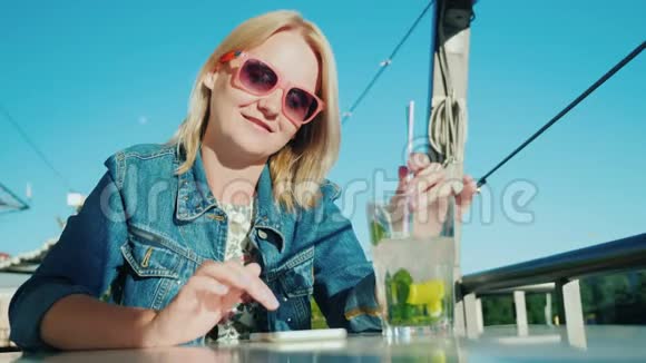 一个女人在咖啡馆里使用智能手机她旁边有一个玻璃杯里面有一杯鸡尾酒休息和商业观念视频的预览图
