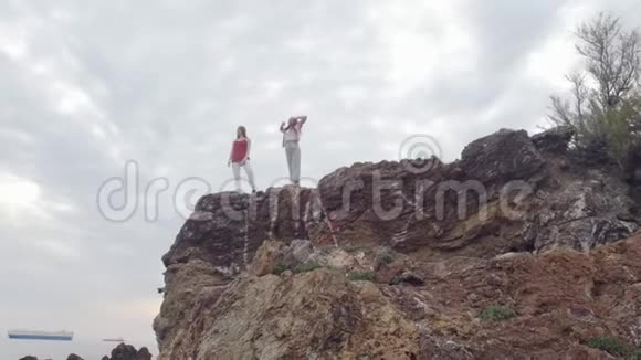 两个年轻快乐的女人在被大海包围的山上走来走去视频的预览图