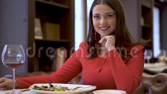 微笑的女人在镜头中摆姿势女士坐在餐厅里喝着红酒和盘子视频的预览图