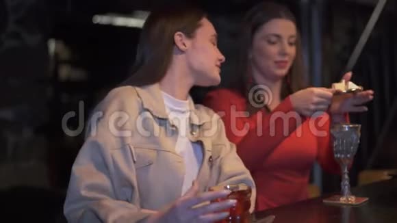 穿红衣服的女人坐在酒吧里手里拿着令人惊叹的设计师设计的金属杯上面放着鸡尾酒和奶酪和其他人交谈视频的预览图