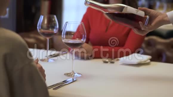 服务员在餐厅里的女孩的杯子里倒红酒女士在微笑两个积极的女朋友坐在一起视频的预览图