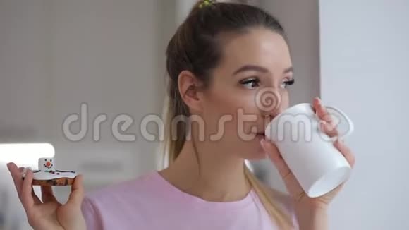 穿着粉红色T恤的年轻女子喜欢在家喝带冬饼的茶视频的预览图