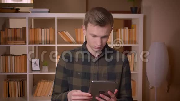 用平板电脑拍摄年轻迷人的白种人男学生的特写镜头并在摄像机中显示蓝色的色度屏幕视频的预览图