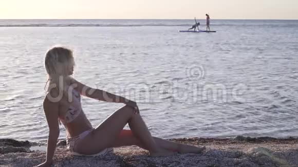 沙滩上穿比基尼的年轻女子正在向镜头挥手五彩缤纷的日落视频的预览图
