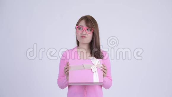年轻快乐的亚洲书呆子女人一边拿着礼品盒思考视频的预览图