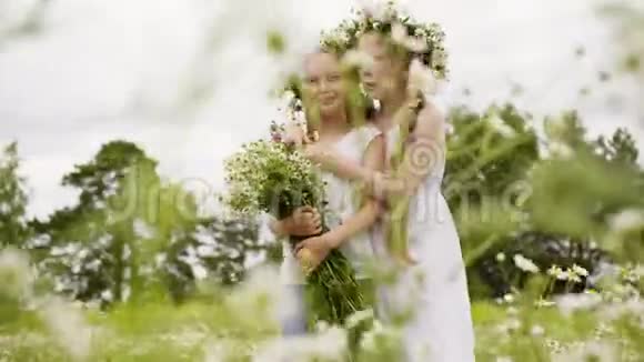 两个少女戴着花圈花束站在盛开的田野上带花束的浪漫女孩视频的预览图