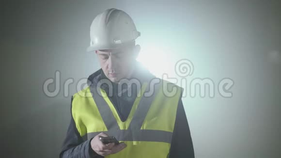 穿着建筑制服和头盔的人在黑色背景前用手机发短信的肖像视频的预览图