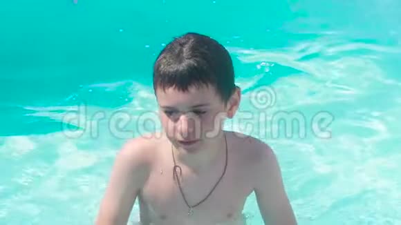 一个脖子上戴着十字架的男孩站在游泳池里清澈的水里里面有漂浮的玩具回到水里视频的预览图