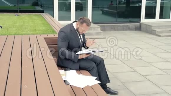焦虑的商人坐在户外的笔记本上寻找东西视频的预览图