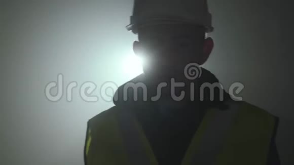 在聚光灯下的黑色背景下工程师穿着建筑制服和头盔走向摄像机的肖像视频的预览图