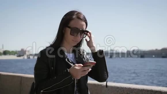 纤细的黑发女孩风吹着她的头发美丽的黑发女子站在桥上靠近河流在城市里视频的预览图