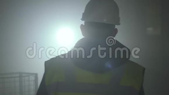 在黑色背景下带聚光灯的背景下穿着建筑制服和头盔行走的人的后景视频的预览图