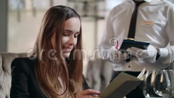 微笑的女人在餐馆里和服务员说话快乐女人阅读菜单视频的预览图