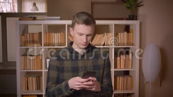 在大学里一位年轻迷人的白种人男学生用手机看着摄像机微笑着拍摄特写镜头视频的预览图