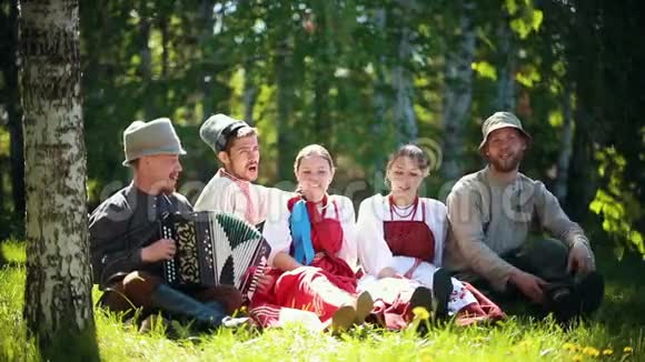 穿着俄罗斯传统服装的人坐在草坪上用手风琴唱歌视频的预览图