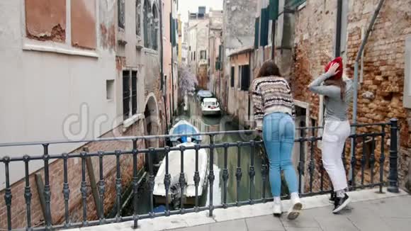 意大利威尼斯两位年轻的女游客站在小桥上在水道上欣赏风景视频的预览图