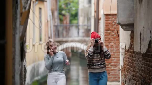 两个年轻的笑女旅行者穿着温暖的衣服站在一个水道的背景上一个女人在和她说话视频的预览图