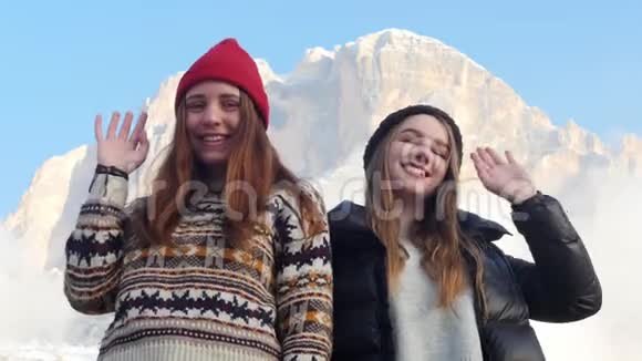 两个年轻的微笑的女人站在一座山的背景上用手挥手视频的预览图