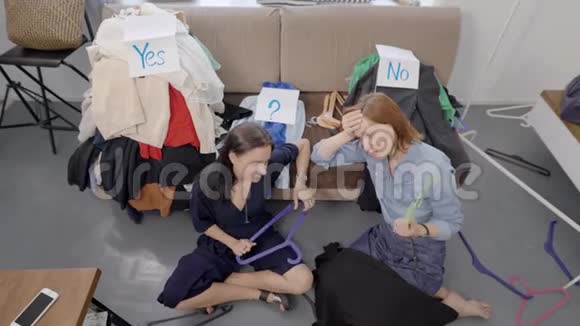 两个疲惫的女人坐在沙发前的地板上从衣柜里整理衣服休息视频的预览图