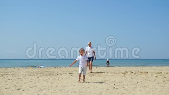 在阳光明媚的日子里妈妈和孩子沿着海边的沙滩散步视频的预览图