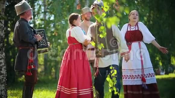 穿着俄罗斯传统服装的人们手牵手在球场上跳舞其中一人演奏手风琴音乐视频的预览图