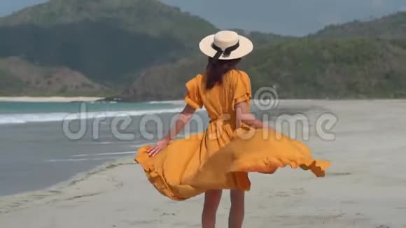 穿着黄色衣服戴着白色草帽的年轻女士在热带度假胜地的海边散步欢快地跳跃着视频的预览图