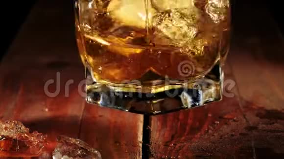 豪华威士忌人慢慢地在玻璃杯里搅动金黄色的威士忌咖啡色的木桌上放着冰块不倒翁威士忌波旁酒视频的预览图