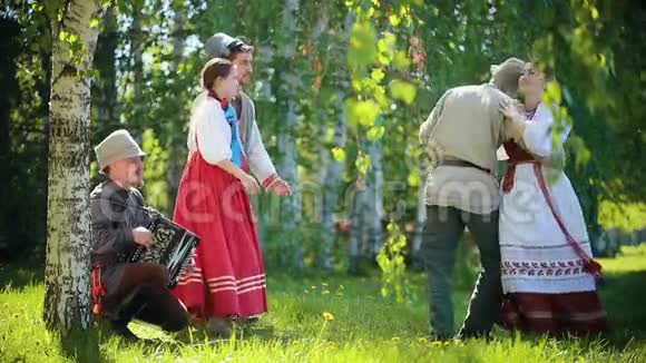 两对穿着俄罗斯传统服装的幸福夫妇用手风琴在田野上跳舞视频的预览图