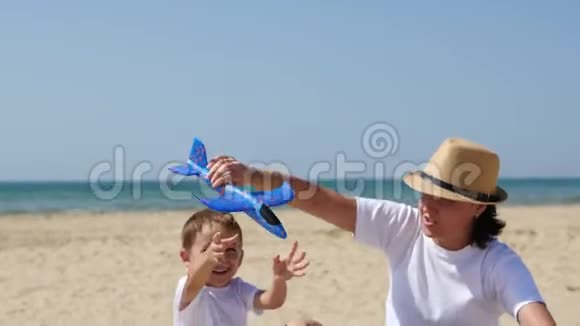 一位快乐的母亲和儿子正坐在阳光明媚的夏日沙滩上慢悠悠地玩着一架玩具飞机视频的预览图