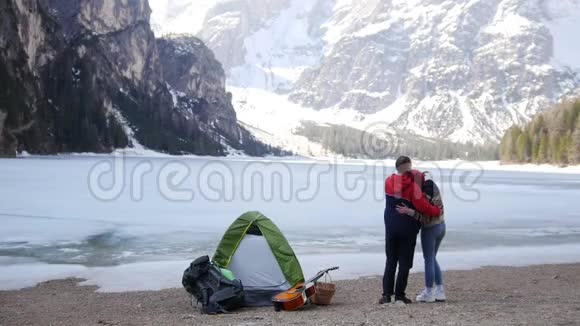 年轻的情侣站在冰冻的湖面上欣赏山景视频的预览图