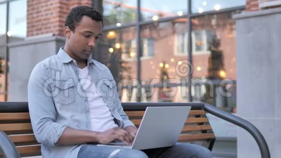坐在室外头痛的非洲男人用笔记本电脑视频的预览图