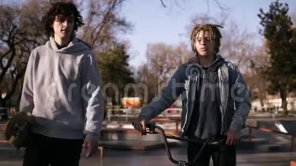 两个朋友滑板车和bmx骑士一起在城市滑板公园散步朋友们在溜冰场交流视频的预览图