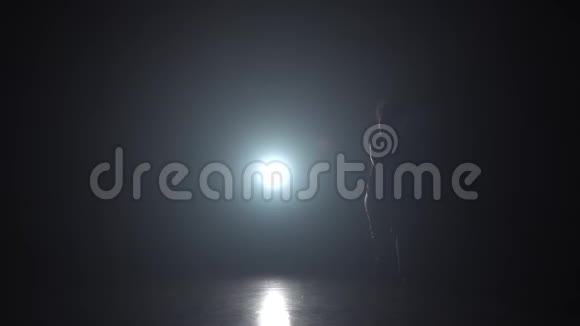慢动作卡波伊拉黑暗中卷曲的女孩在灯光照射下的剪影视频的预览图