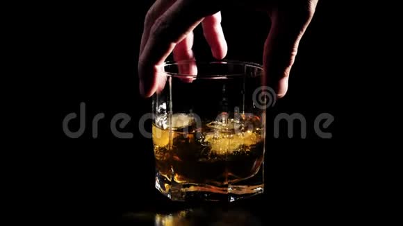 豪华威士忌手拿一杯带有冰块的金色威士忌放在黑色的桌子上背景是黑色的视频的预览图