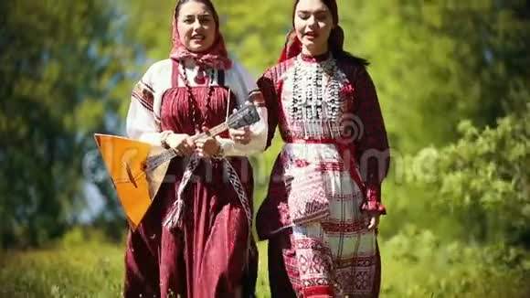 两个穿着俄罗斯传统服装的年轻女子在森林里散步唱着一首歌其中一个抱着巴拉莱卡视频的预览图