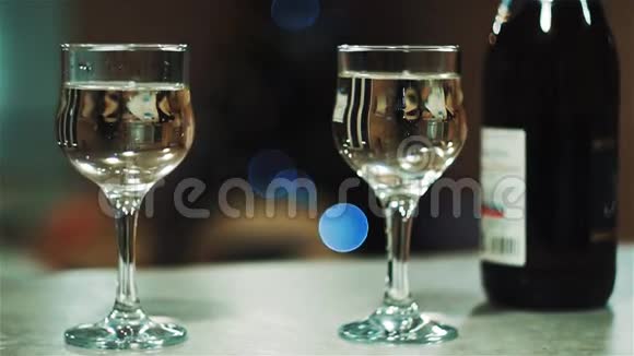两杯桌上放一瓶香槟彩灯圣诞树背景视频的预览图