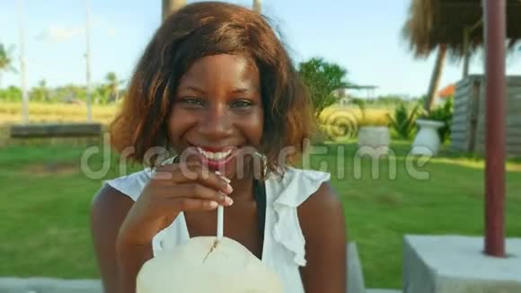 年轻快乐迷人的黑人美国妇女躺在热带度假花园里喝椰子水视频的预览图
