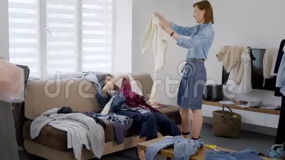 疲惫的女客户穿着一堆衣服躺在沙发上她的形象师站在旁边拿着礼服视频的预览图