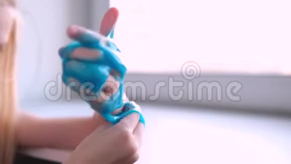 一个女孩把蓝色的黏液伸向两边孩子们玩粘液玩具在白色上做黏液时尚液体玩具棒视频的预览图