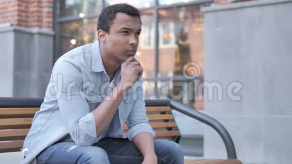 穿着衣服头痛的非洲男人坐在户外视频的预览图