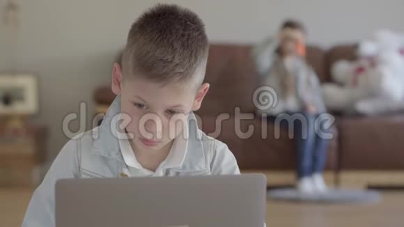 小男孩坐在笔记本电脑上小女孩他的孪生妹妹在家里的沙发上吹肥皂泡视频的预览图