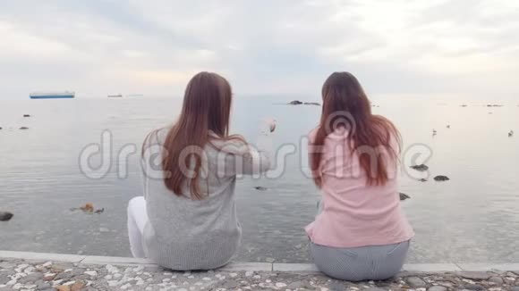两个年轻的女朋友坐在靠近大海的楼梯上视频的预览图