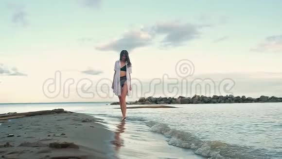 穿着短裙子和泳衣的女孩赤脚在沙滩上散步视频的预览图