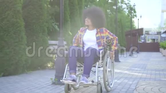 在阳光明媚的公园里戴着非洲发型的非洲女人坐着轮椅戴着眼镜骑着车视频的预览图