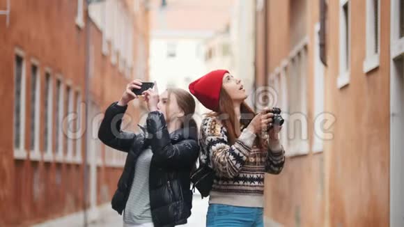 两位穿着保暖衣服的年轻女性旅行者走在意大利狭窄的街道上用相机拍照视频的预览图